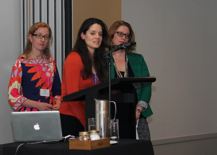 a trio of women stand behind a podium