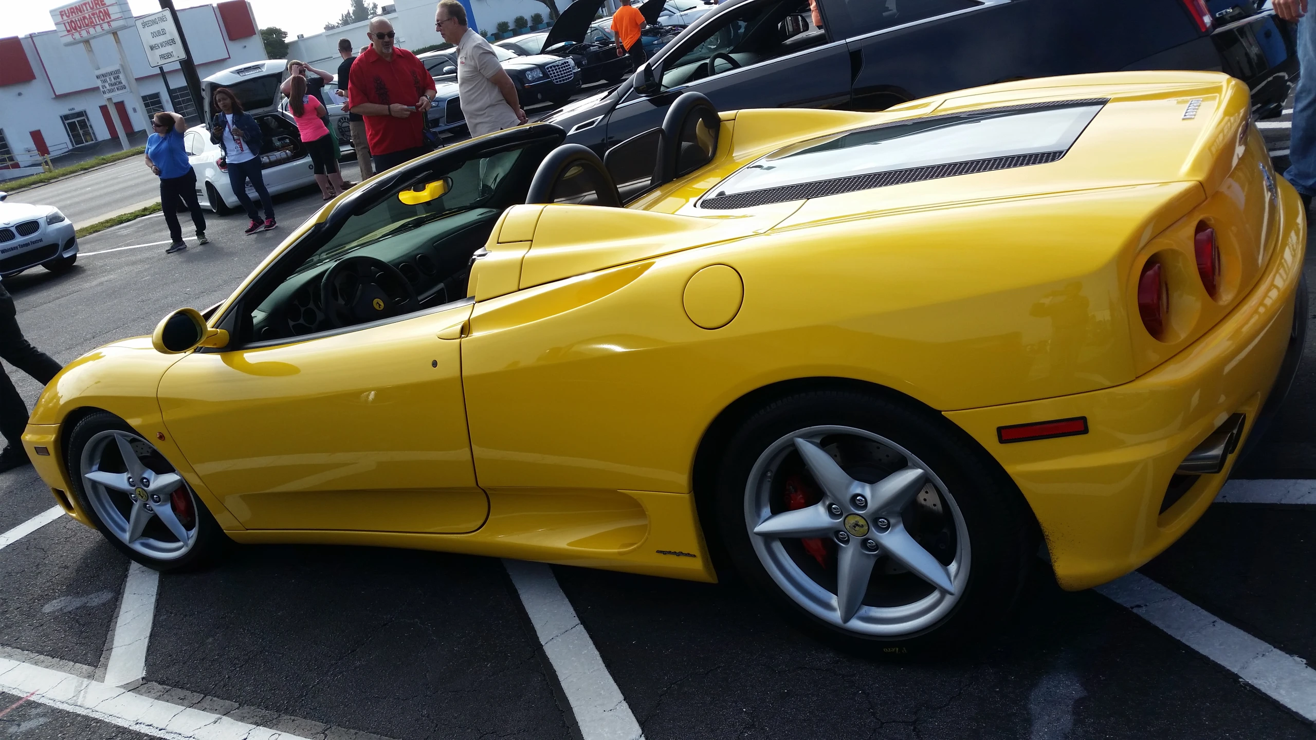 people gathered around some cars parked in the parking lot