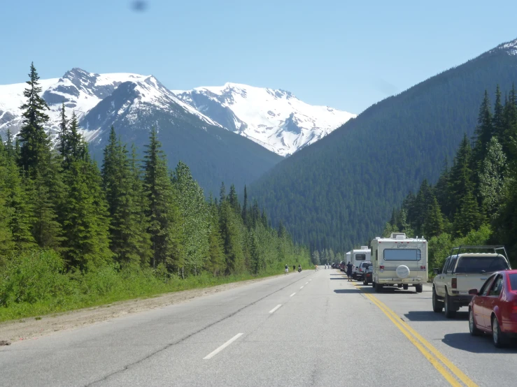 trucks driving down the road next to trees and mountains