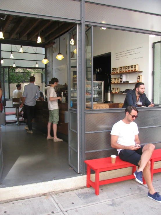 a man sits on a bench as others look in the shop