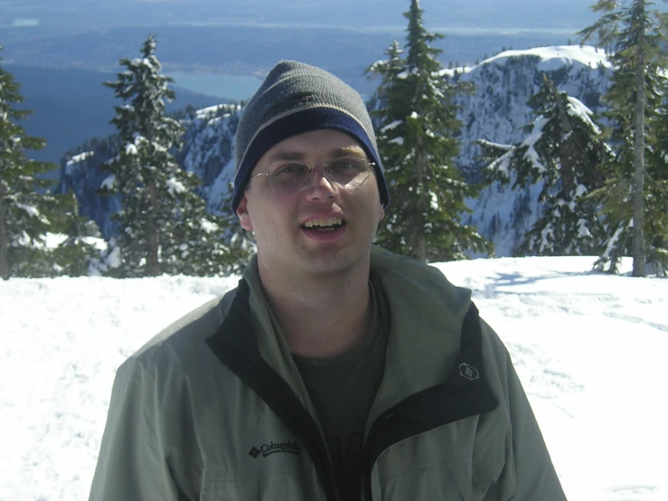 the man smiles in the foreground while standing at the top of a snowy mountain