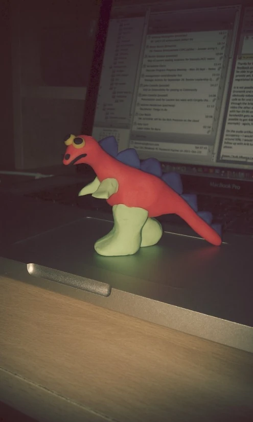 small plastic toy dinosaur walking across a laptop computer