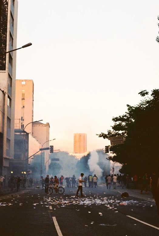 many people on the street with some buildings and smoke in the air