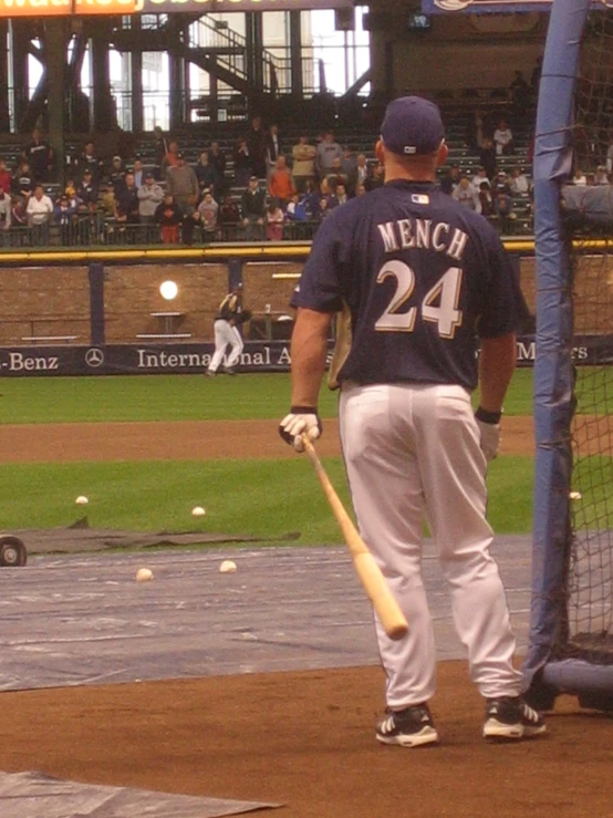 man in baseball uniform holds a bat near home plate as audience watches