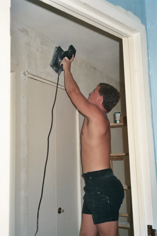 a young man in black underwear brushing his hair with a power tool