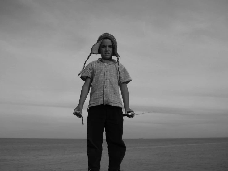 a boy wearing a hoody and flying a kite near the ocean