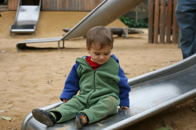 a small boy sitting on a slide near a child's play ground