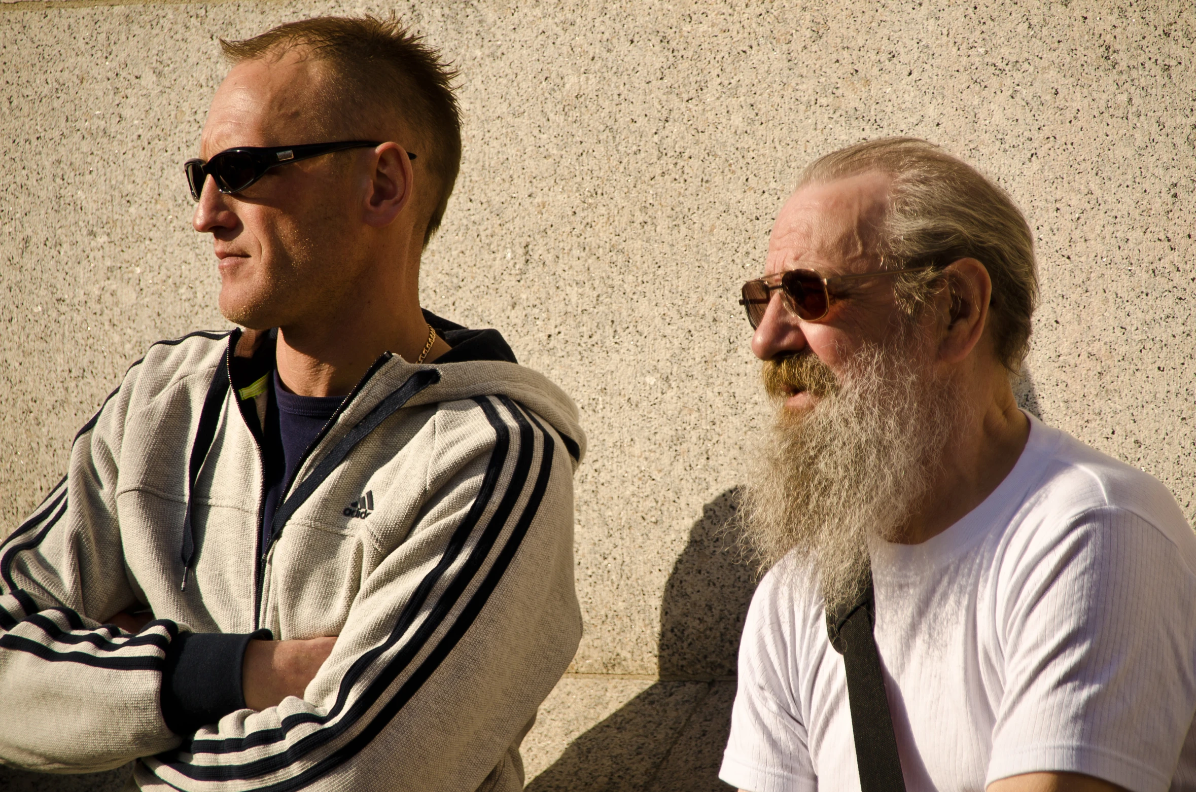 two old men sit side by side with their arms crossed