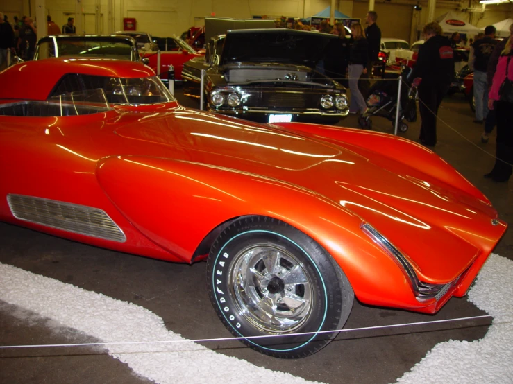 an orange, vintage style, car is parked in a garage with people