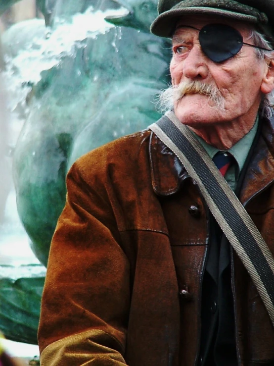 an older man sitting in front of a fountain wearing glasses and hat