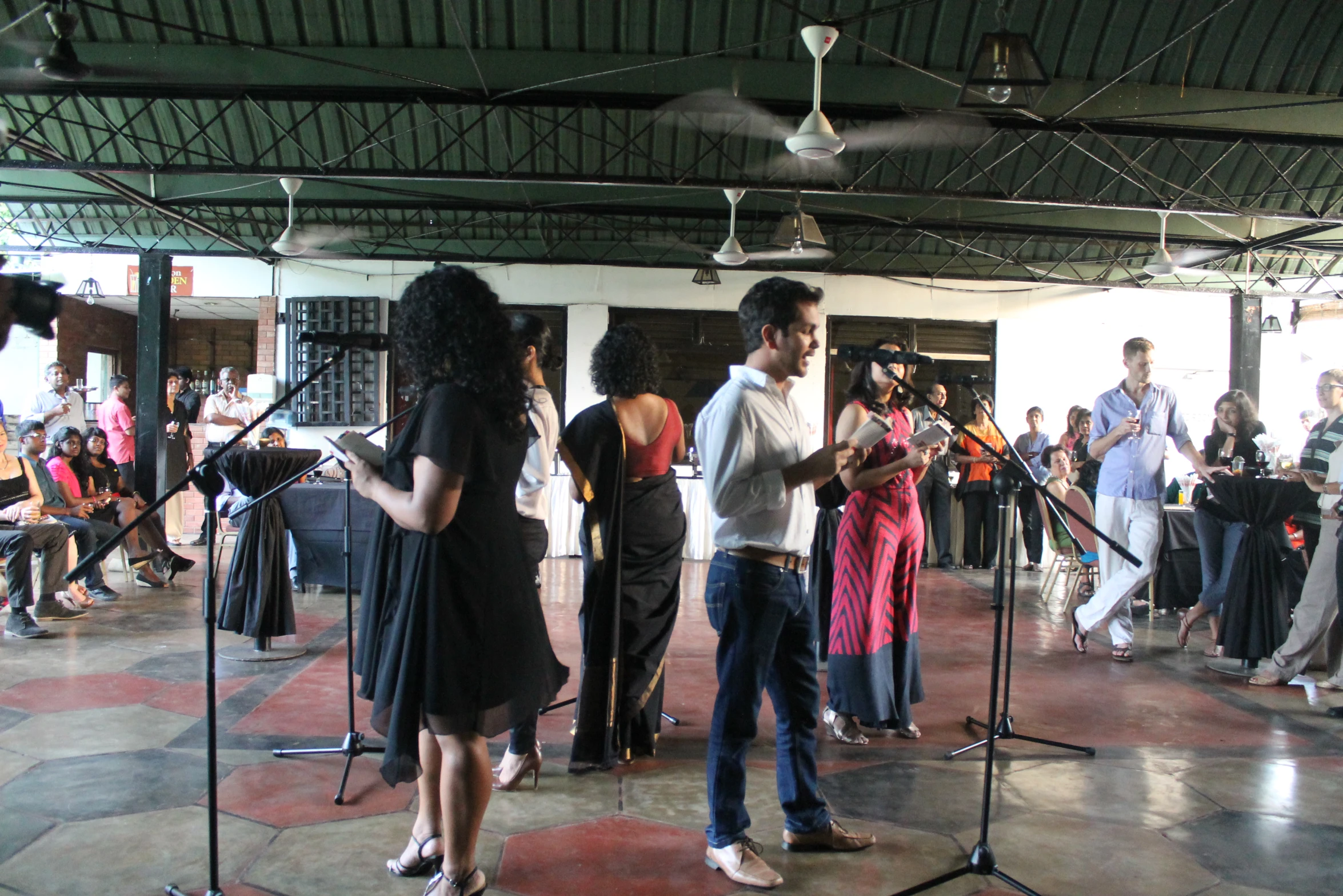 several people performing in an empty room, many singing and one is looking down on soing