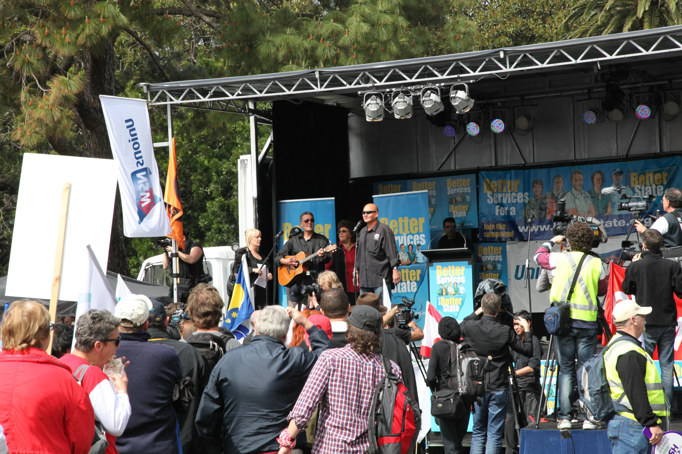 a band on stage at the park, with spectators standing around