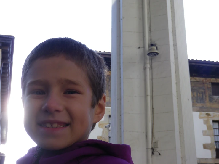 a close - up of a little boy wearing purple with a building in the background