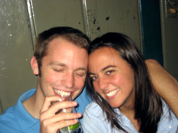 a man and woman smile for the camera as they hold glasses with green liquid in their mouths