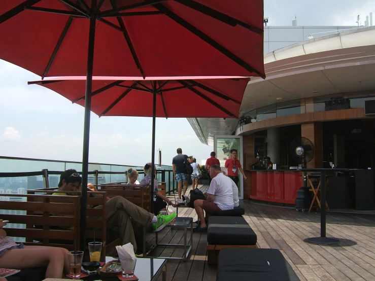 people sitting outside on benches with tables under an umbrella