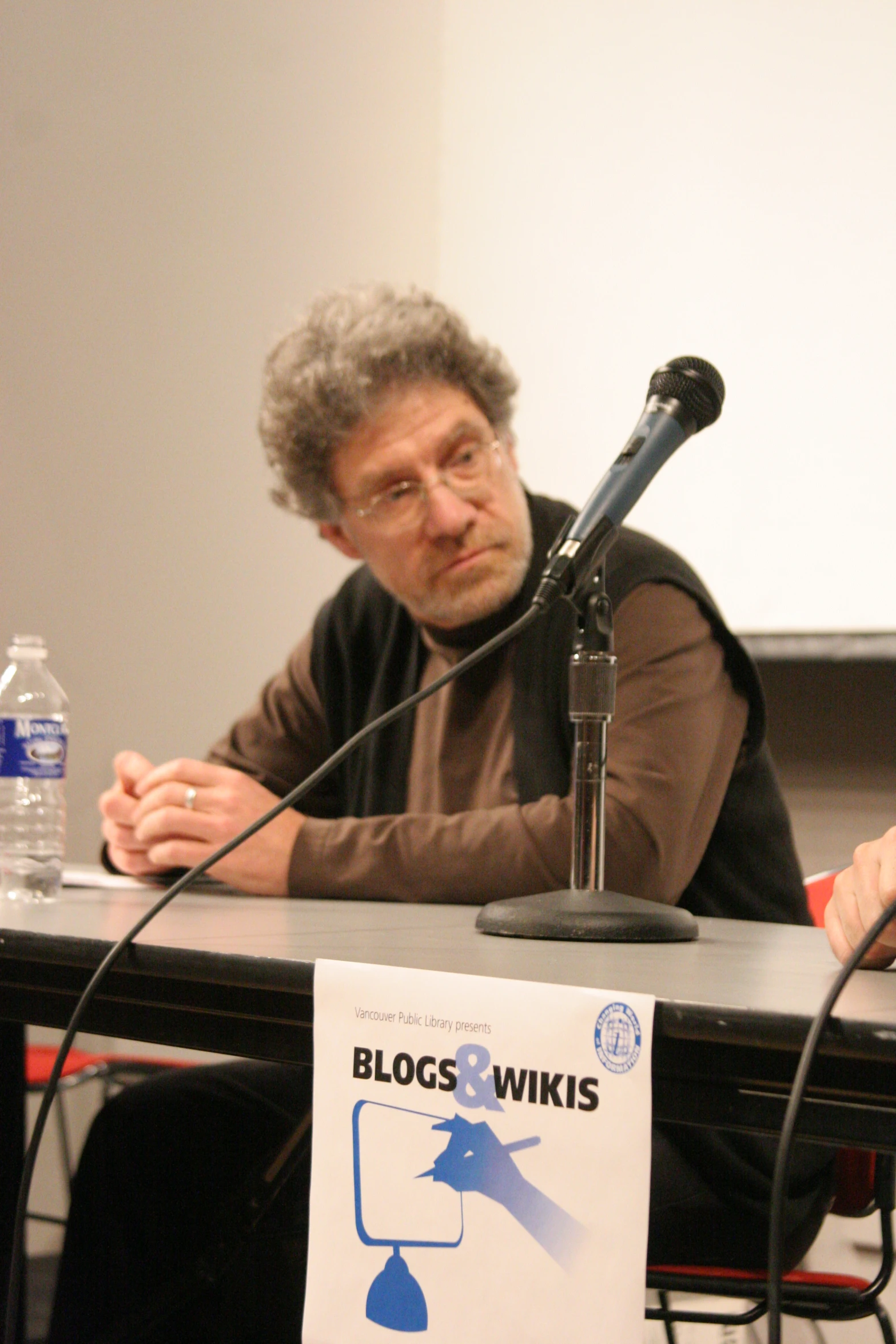 a man with curly gray hair sitting at a table in front of a microphone