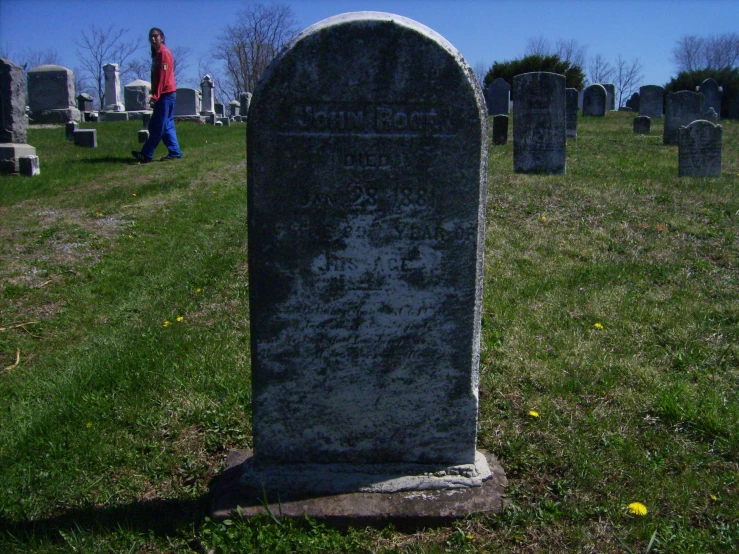 a young man walking towards the headstone of a very old grave