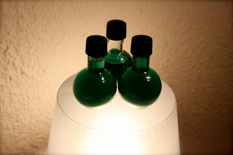 three green vases with black tops are on a table