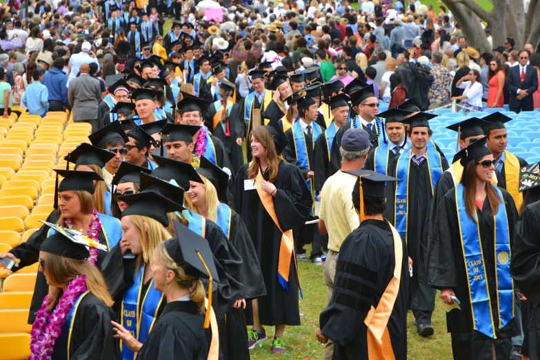 a large graduation crowd is standing together in the grass