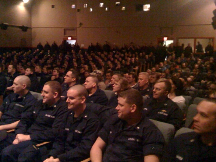 some men in uniforms are sitting on chairs in front of an audience