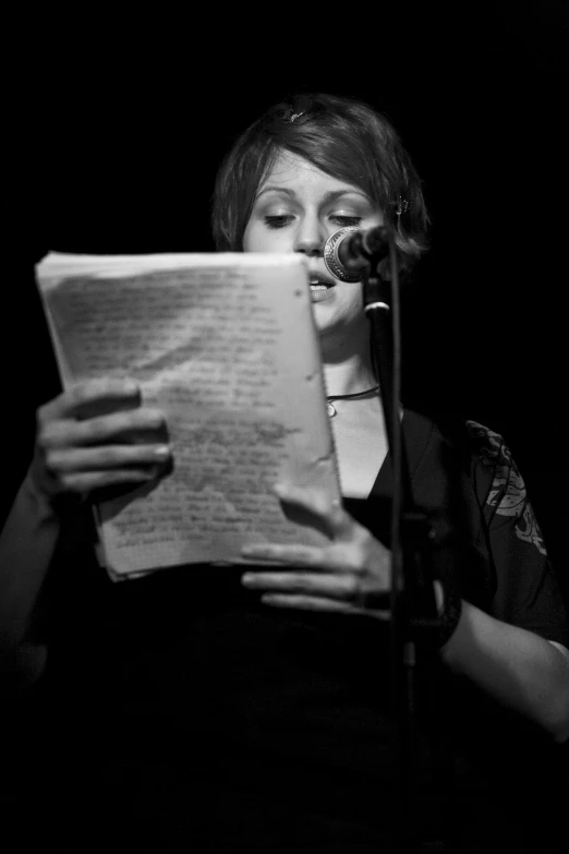 a woman reads while standing in front of a microphone