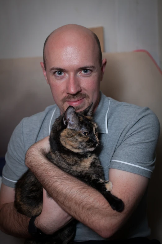 a bald man holding a cat, looking at the camera