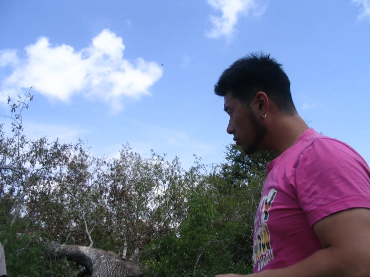 a man in a pink shirt with a cellphone near trees