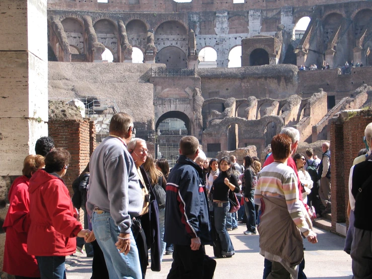 people stand in a courtyard near a wall of the colliseum