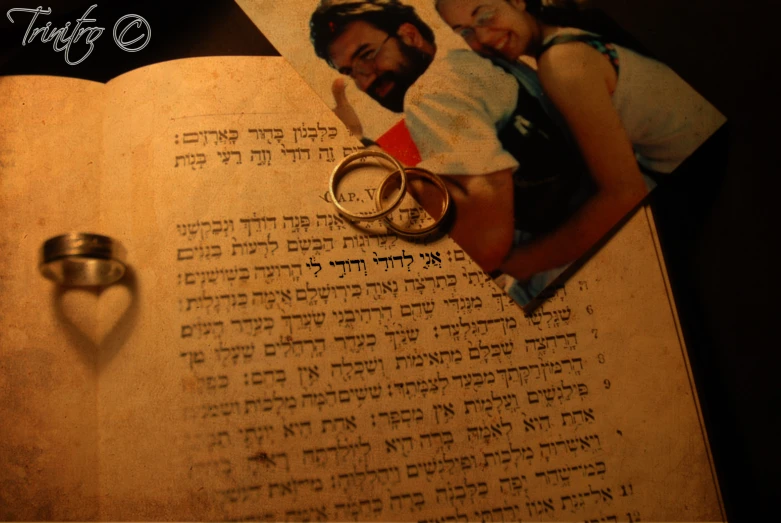 an open book has a picture of two people, with two wedding rings next to it