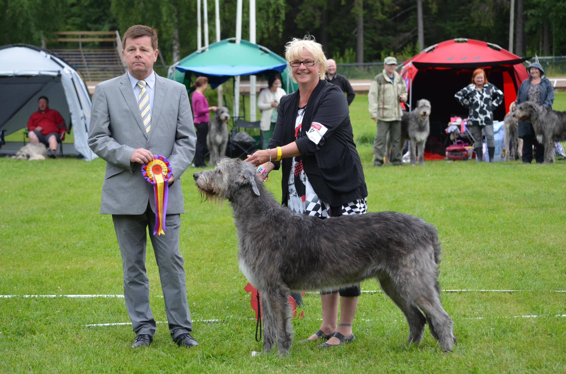 two women holding a large black dog in a green field