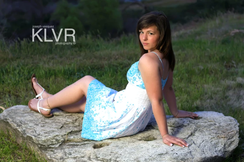an attractive young woman in a blue dress laying on a rock