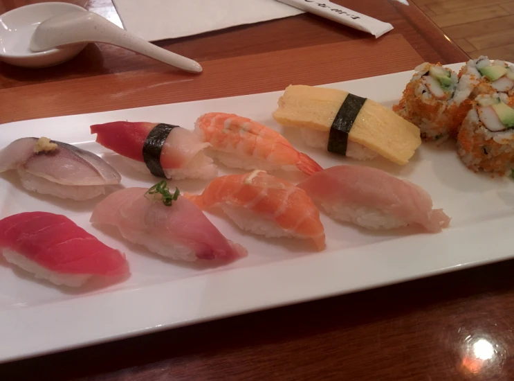 assorted sushi on a plate next to dipping spoon