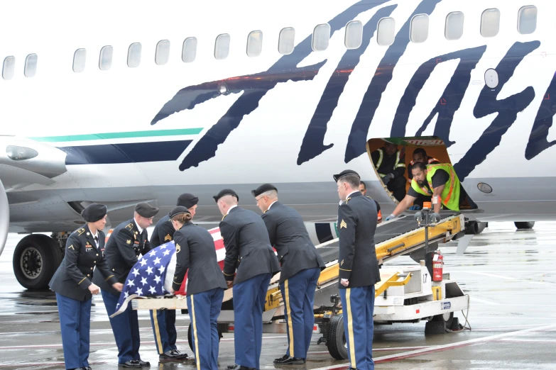 several men in military uniforms standing at the loading stairs to a large air plane