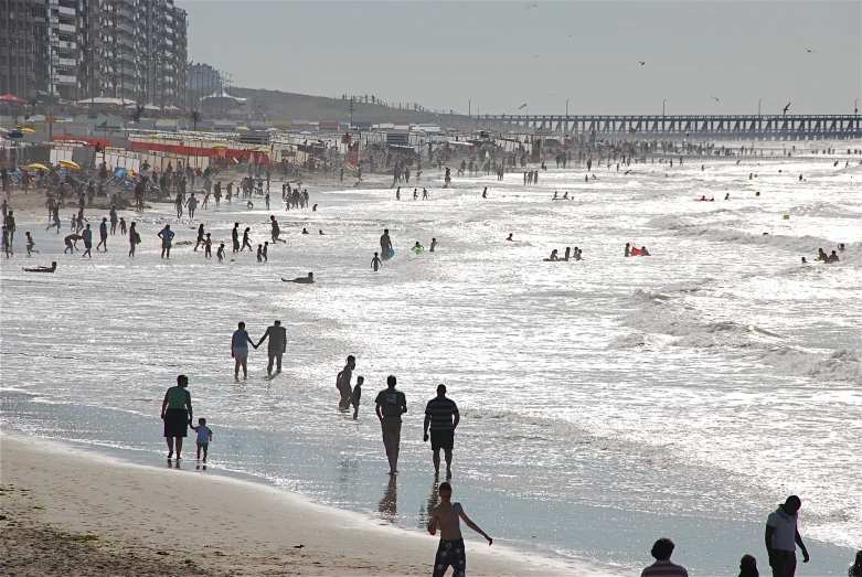 people are standing on the beach, in front of a pier