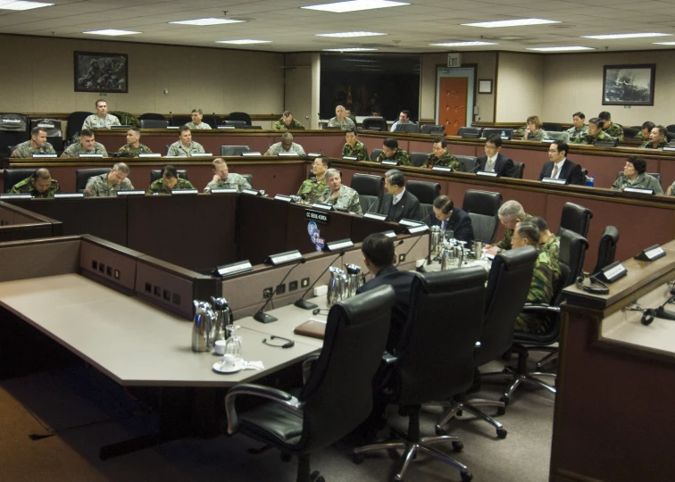 a large group of men in uniform sitting in a large table with a bunch of laptops