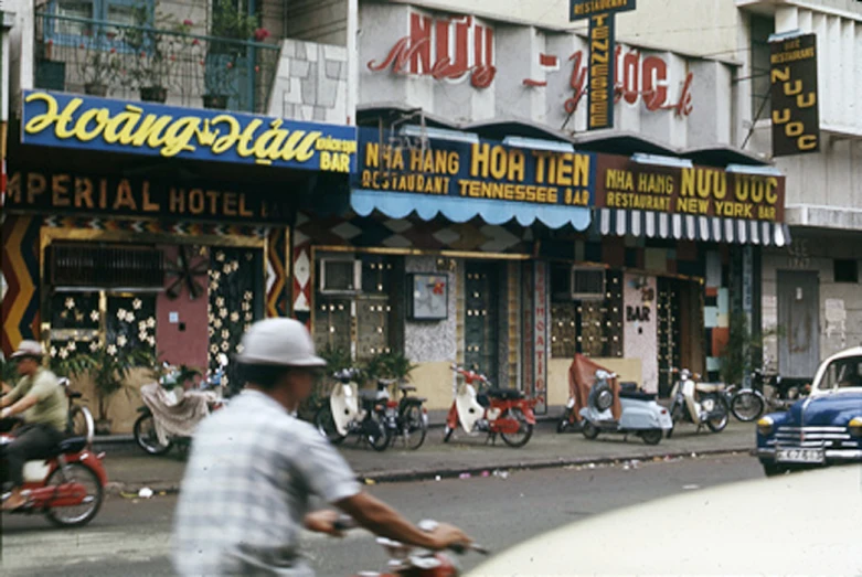 people walking, bikes and cars in front of stores in an asian town