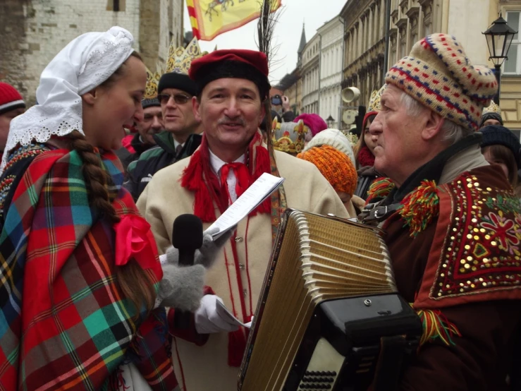 a man in a kilt with an accordion and two women holding a microphone