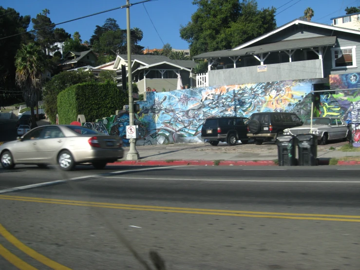 the cars are traveling through a neighborhood near a graffiti covered wall