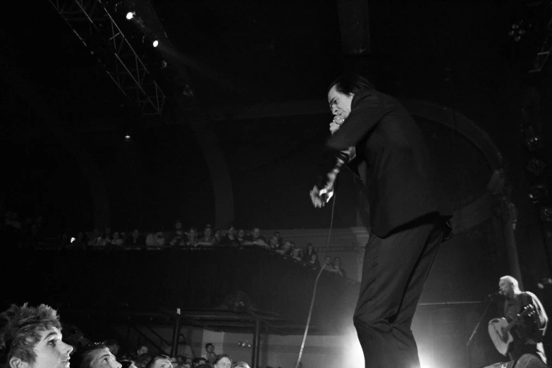 a black and white pograph of a man on a stage while other people watch