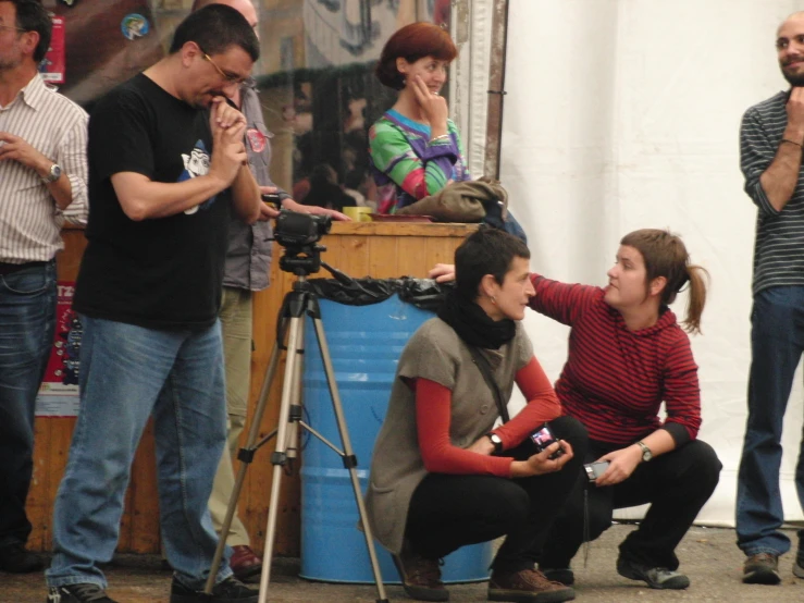 people stand around while a woman sits in front of a camera