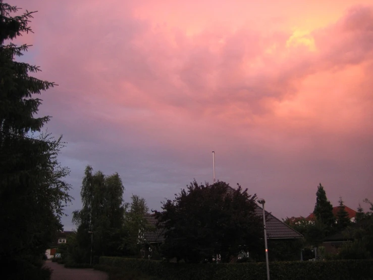 a large pink cloud in the sky above some trees