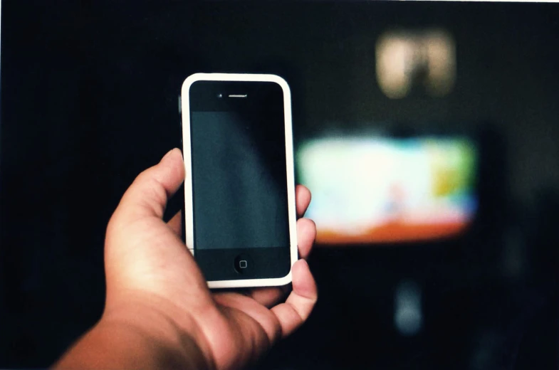 person holding cell phone up to television screen