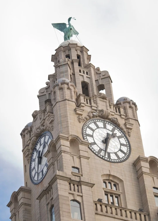 the tower clock features a winged statue and large white clocks