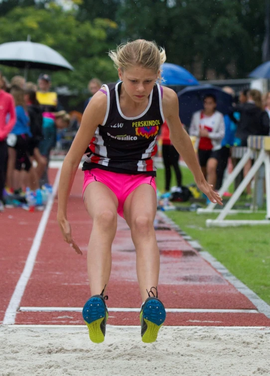 a  in pink shorts and blue shoes jumping on a race track