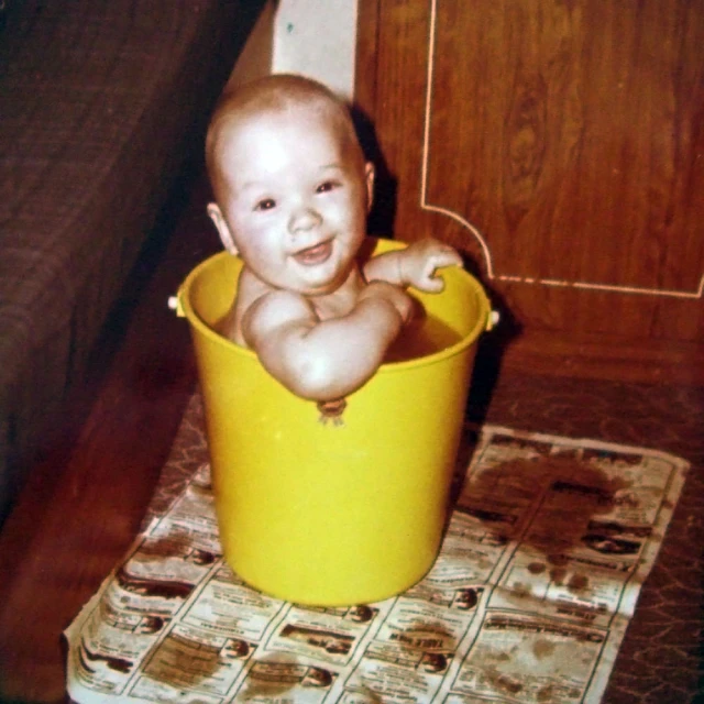 baby in yellow bucket with white top sitting on floor