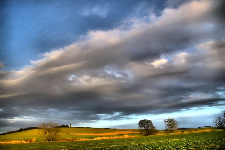 a green grassy field surrounded by trees and clouds