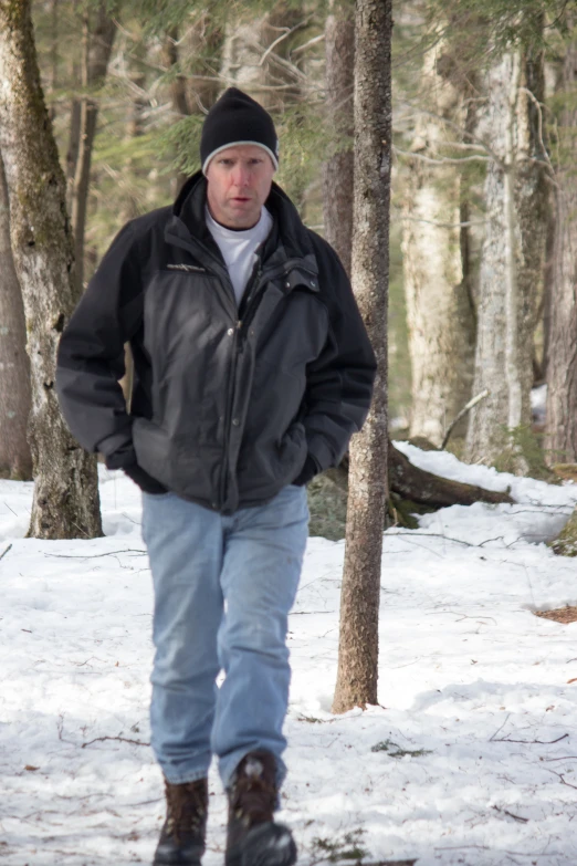 a man in a jacket and beanie stands next to a tree in a snowy forest