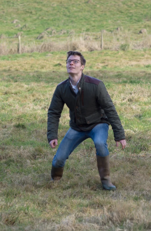 man on grass with boots and jacket on taking a picture