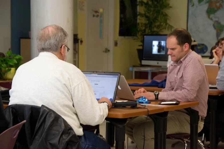 two men sitting at a table using laptop computers