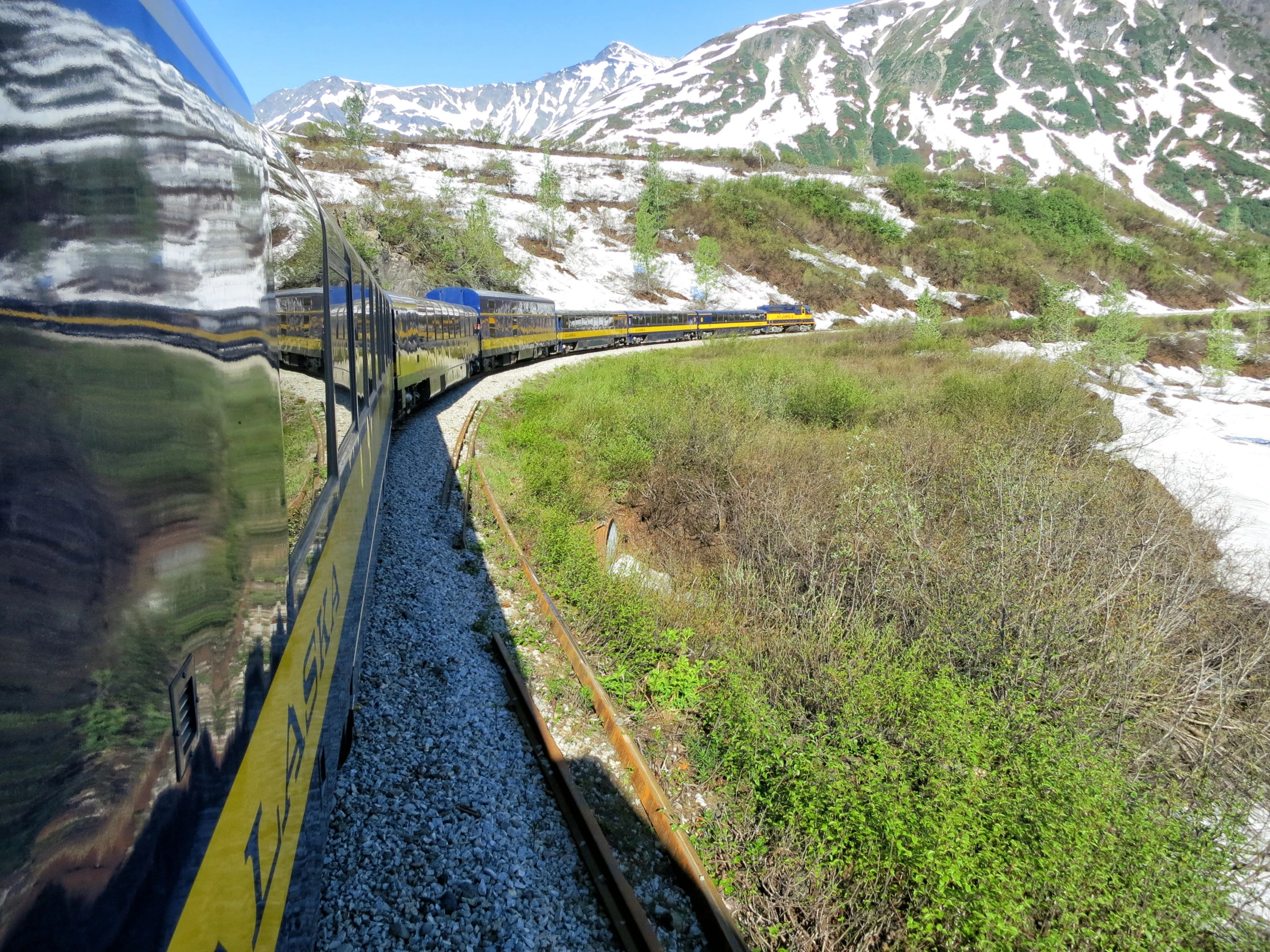 a very long train moving along a train track by a snowy mountain